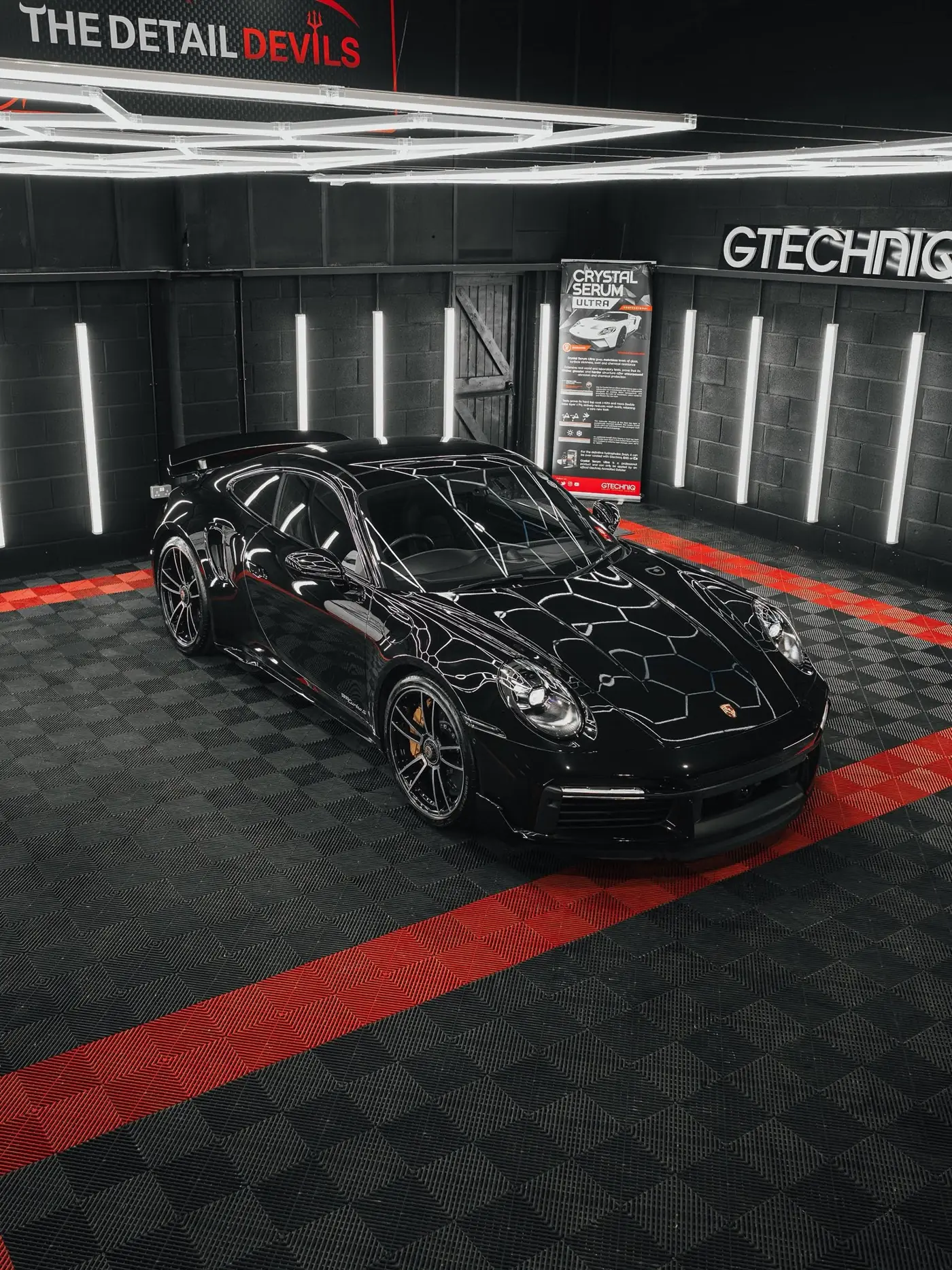 Black Porsche 911 Turbo S under hexagon inspection lights inside The Detail Devils unit